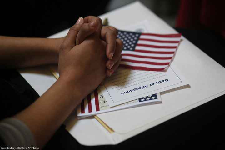 A participant folds her hands of a copy of the Oath of Allegiance and an American flag while listening to speeches during a naturalization ceremony