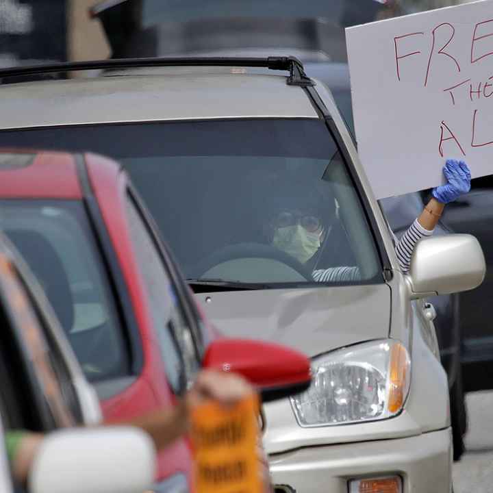 A demonstrator holds a sign with the text "Free Them All" in a car-based protest to demand the release of immigrants in California detention centers over COVID-19 concerns.